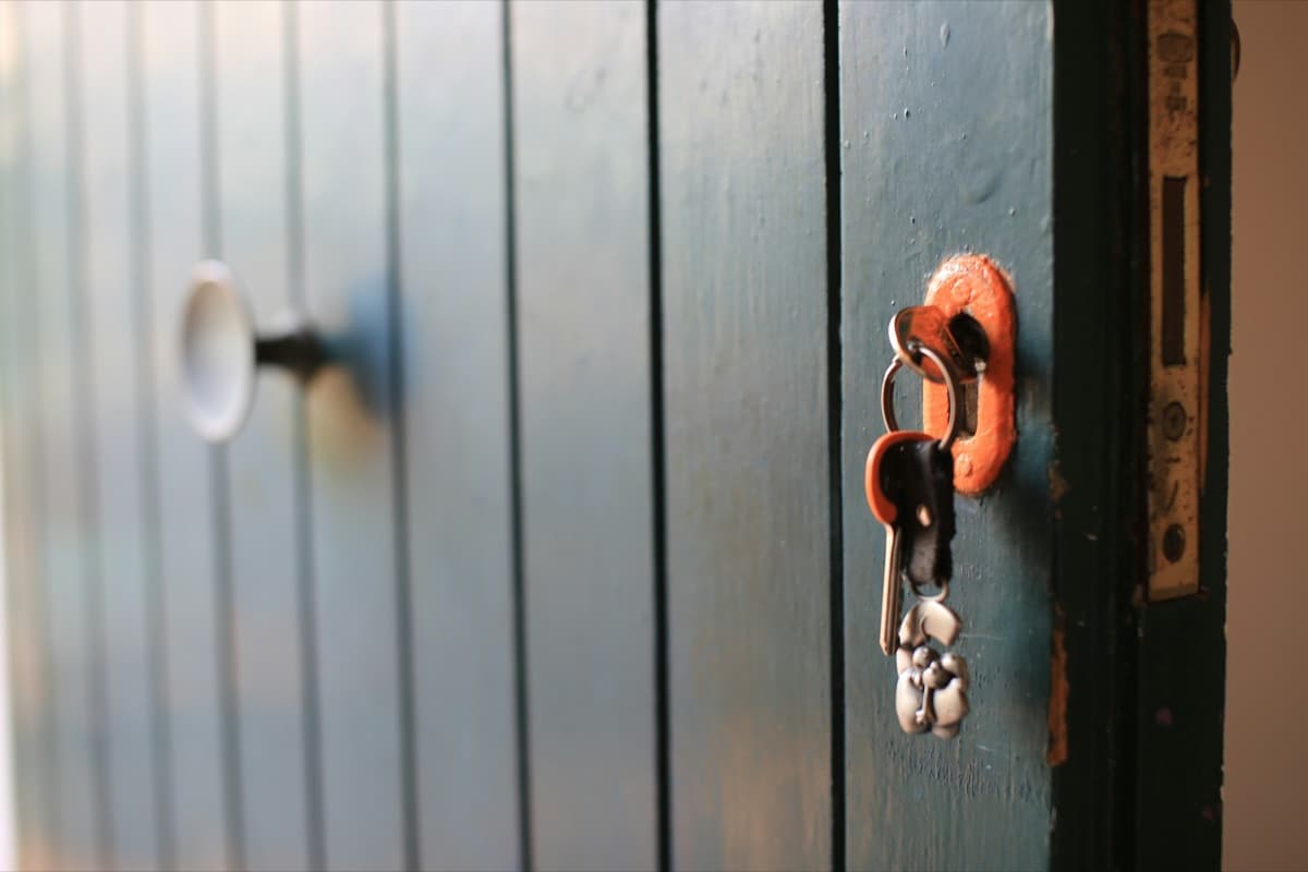A bunch of keys hanging in the lock of a green wooden door, in warm light.