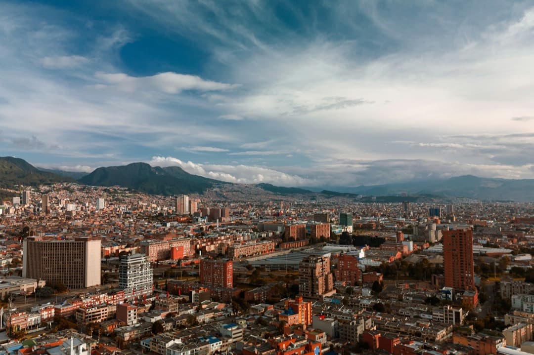 Aerial view of Bogotá in late-afternoon light, with brick buildings and mountains under a wide sky.