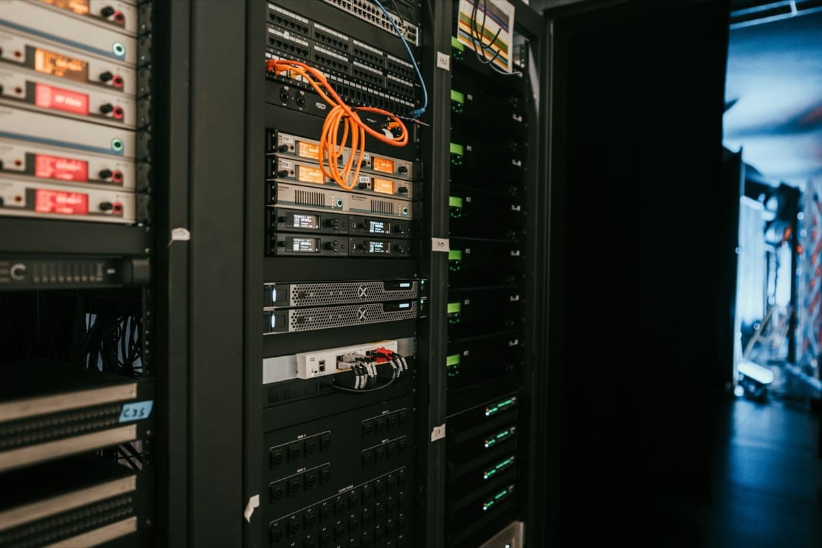 A rack of network equipment in a technical room, with status lights on and an orange patch cable.