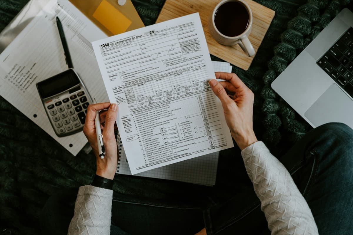 Hands reviewing a financial form next to a calculator, a notebook and a cup of coffee.